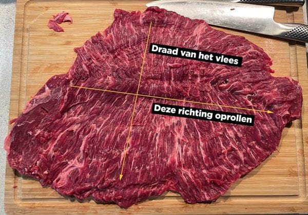 Een gevlinderde bavette op een snijplank waarin staat aangegeven hoe de draad van het vlees loopt en in welke richting de rollade opgerold moet worden.