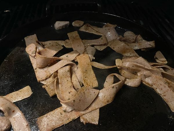 Dun gesneden slierten frikandel met shoarmakruiden die worden gebakken op een hete plancha