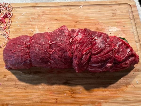 Een opgeknoopte bavette rollade op een snijplank gevuld met verschillende ingrediënten.