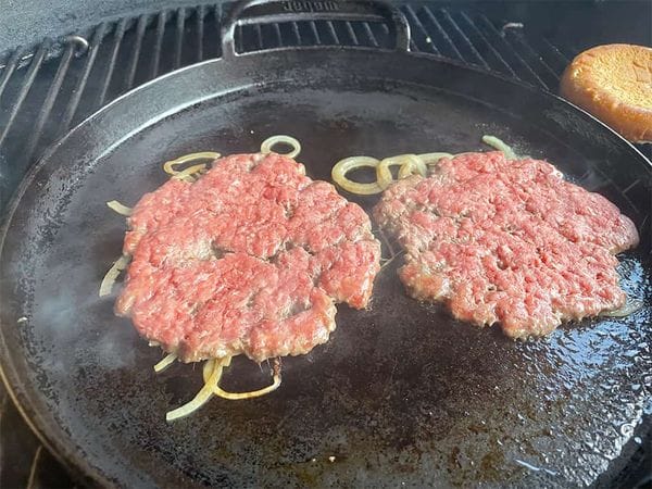 platgedrukte smashburgers met ui op een grilplaat