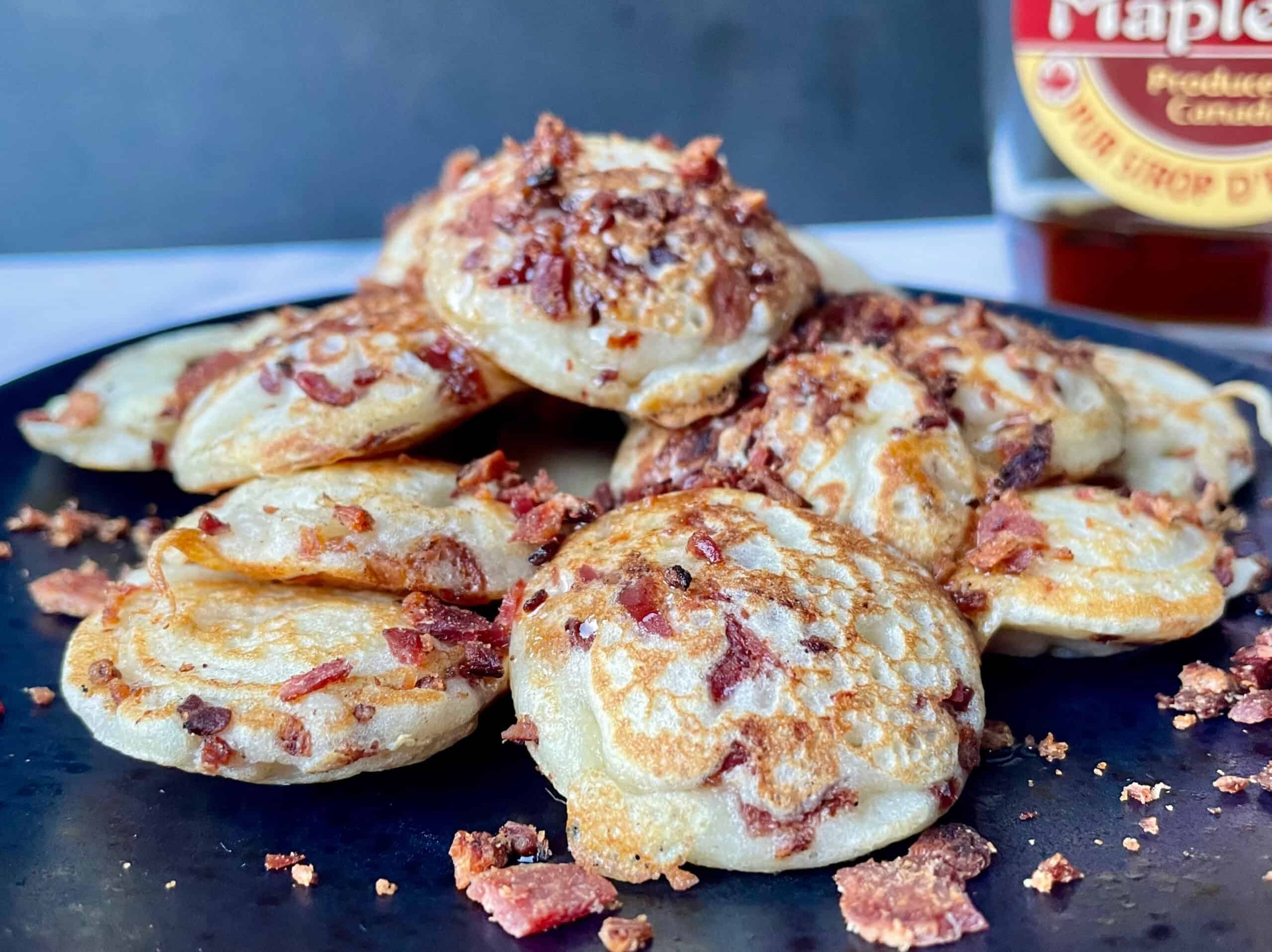 Poffertjes met bacon en ahornsiroop op een zwart bord